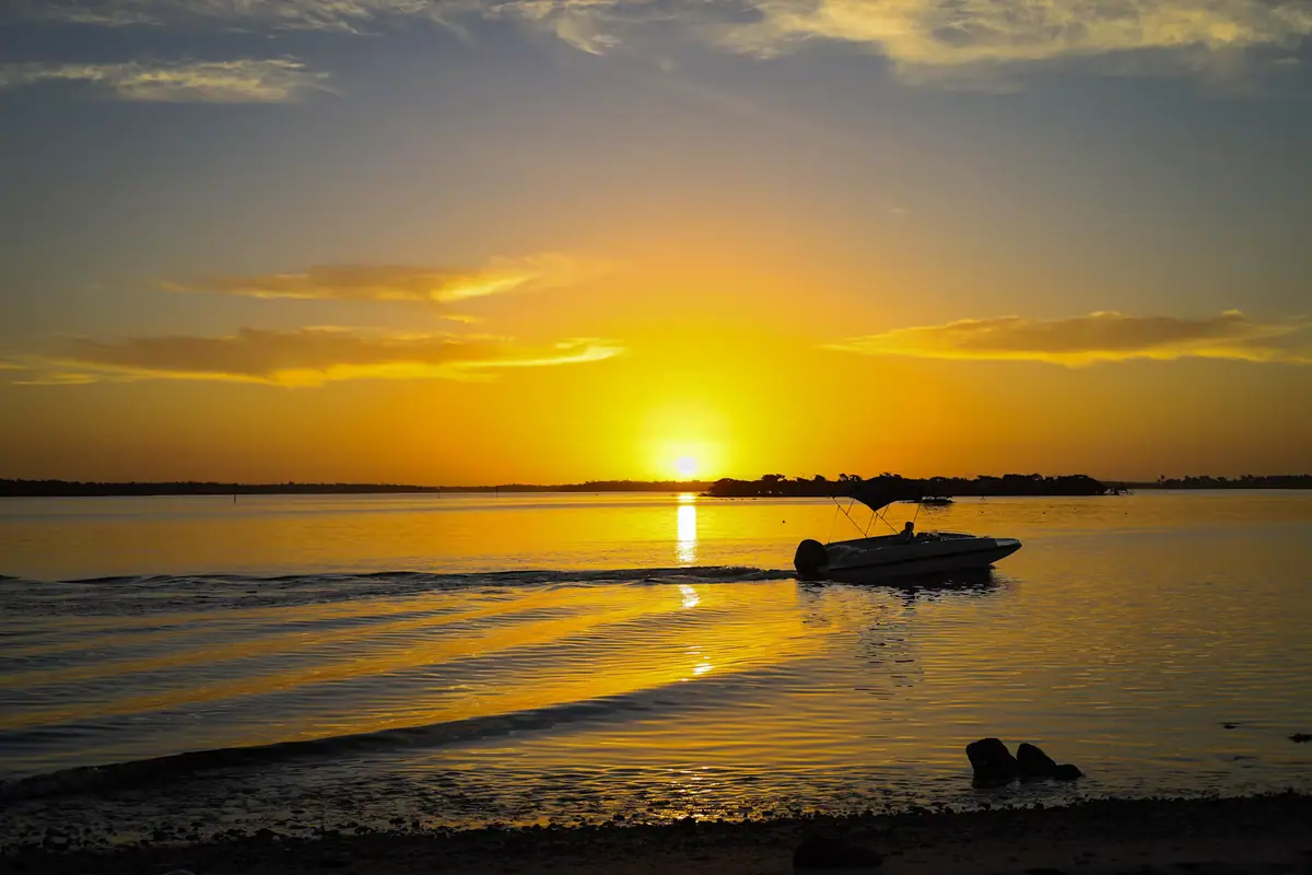The sun low over open water with a small boat silhouetted against the light