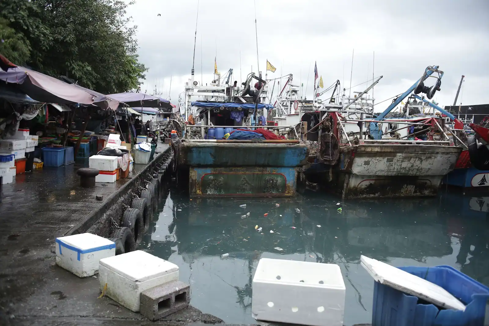 Working fishing boats moored along a harbour dock under a heavy overcast sky
