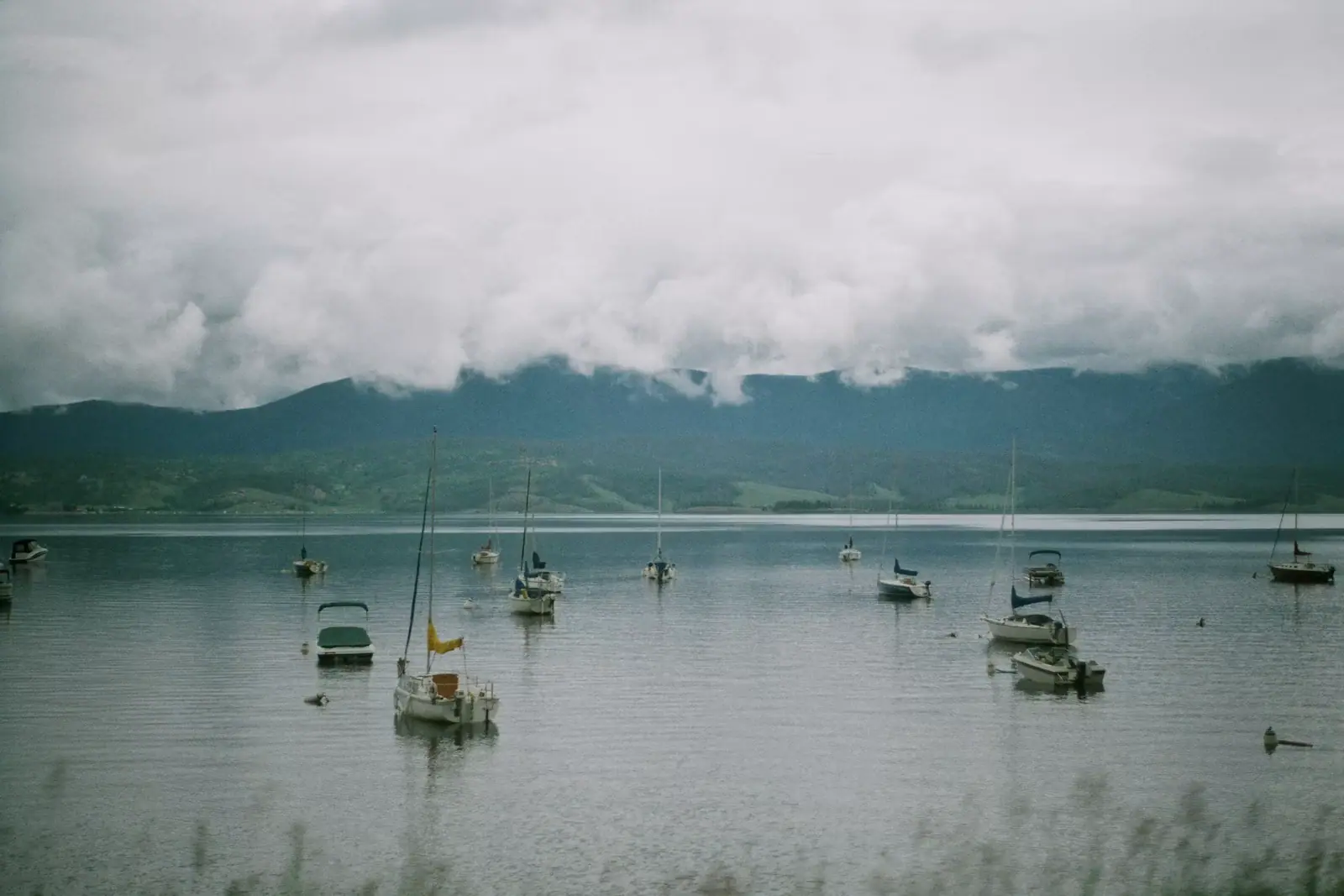 Small boats lying at anchor on flat grey water under a heavy cloud-filled sky