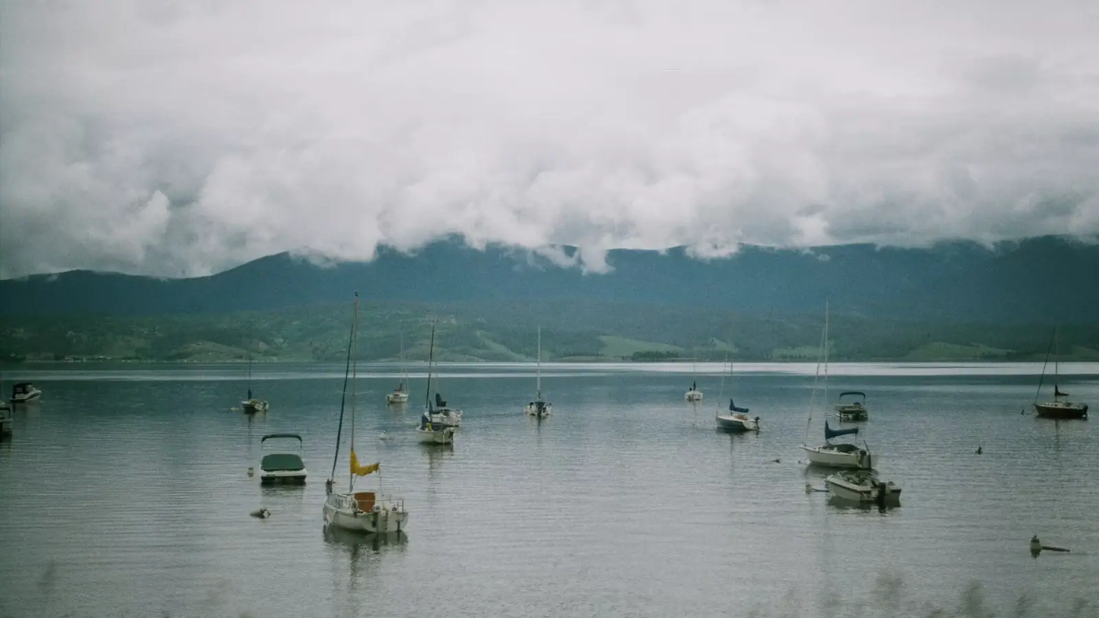 Small boats lying at anchor on flat grey water under a heavy cloud-filled sky