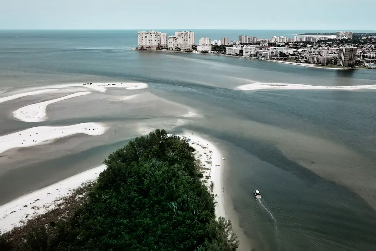 Aerial view of a narrow tidal pass cut between two low sandy shorelines
